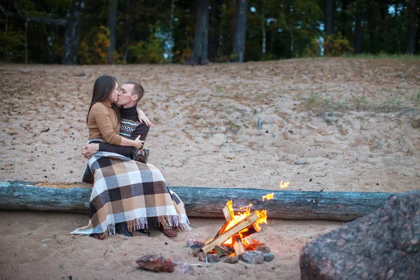 Loving couple sitting on a log by the fire on the beach