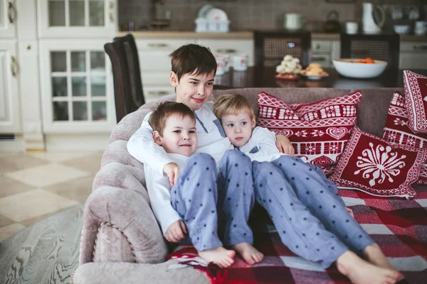 Three young brothers in identical pajamas sitting on a sofa