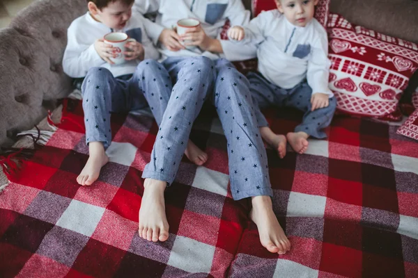 Legs young brothers in identical pajamas holding mugs of milk sitting on a sofa
