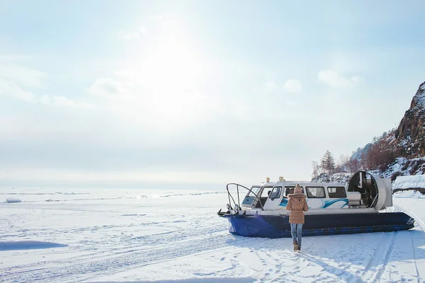 Girl walking on the frozen Lake in the side of the boat hovercraft