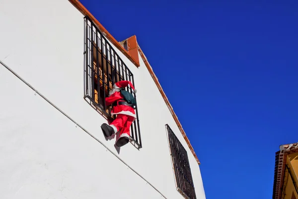 Santa Claus climbing up a wall into a window.