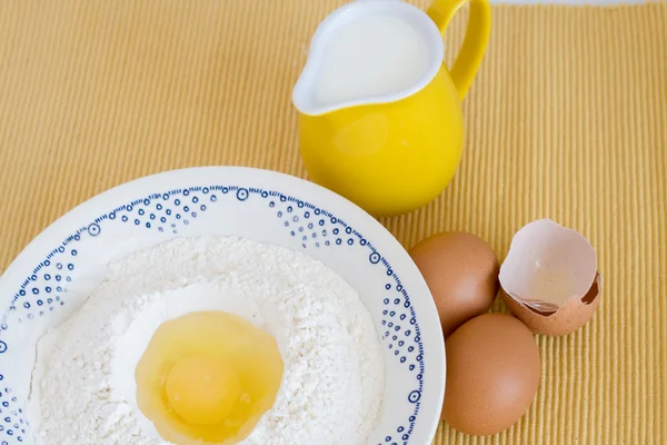Plate with flour, eggs and milk jug standing on a yellow backgro