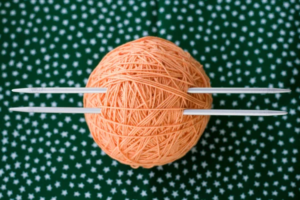 A bright orange ball of yarn and needles for knitting lying on a