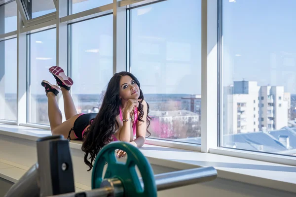 At gym. Athletic brunette posing on window sill