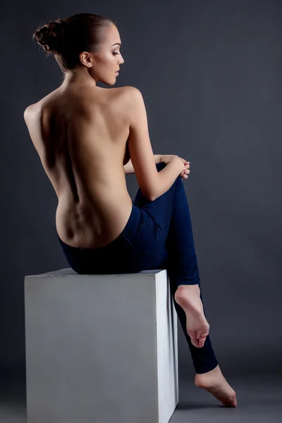 Topless model posing sitting on cube. Back view