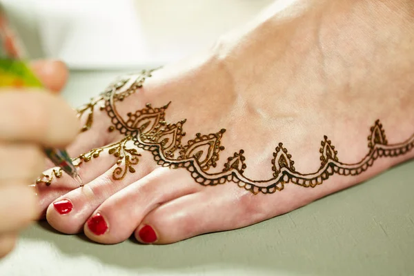 Mehendi. Master applying henna on models leg