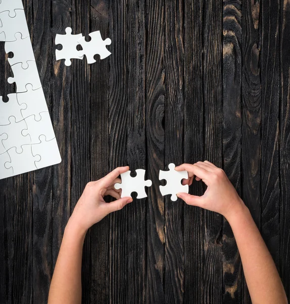 Hands holding pieces of white puzzle on dark table