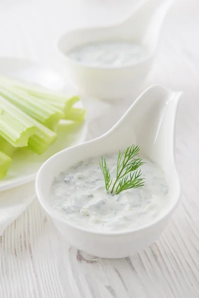 Fresh celery sticks with yogurt dip on white wooden background