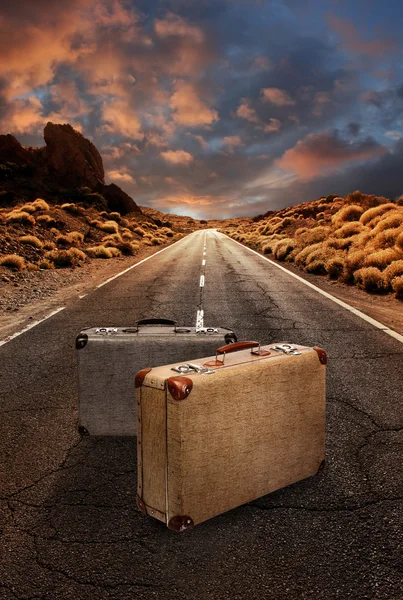 Two vintage suitcases on road through desert