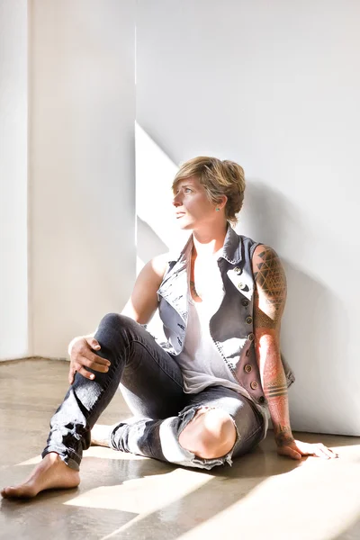 Woman with tattoo sitting on the floor and looking away