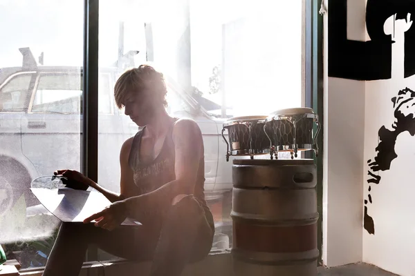 Girl with a tattoo reads a vinyl album in sunlight