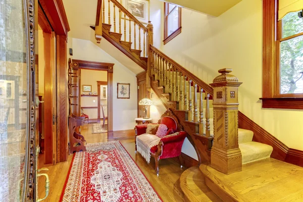 Bright hallway with colourful rug, nice red sofa, wooden stairca