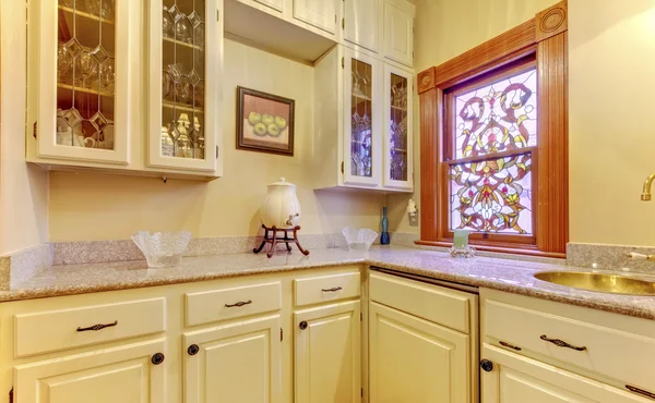 Kitchen area with marble top, cabinets and stained glass window
