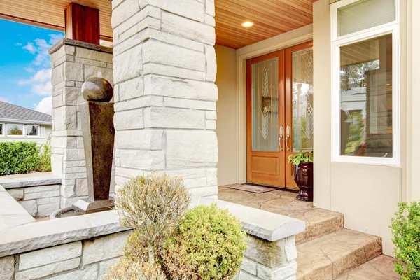 Luxury house entrance porch with stone column trim and stained wood door.
