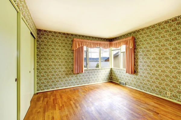 Empty room with hardwood floor, green walls decorated with floral patterned wall paper.