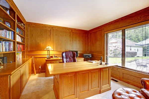 Interior of the wooden cabinet in the American style with desktop, bookcase and brown leather chair.