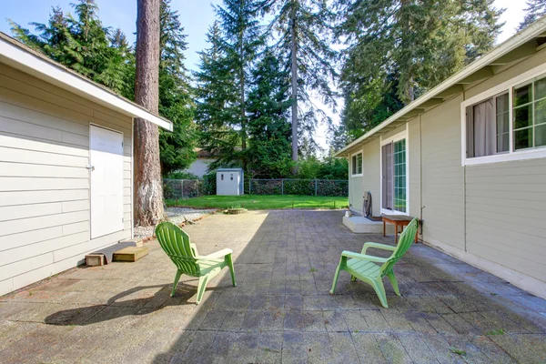 Backyard deck with tile floor and two green chairs