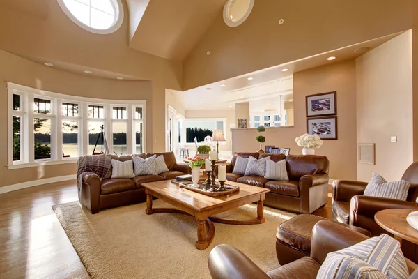 Large living room interior design with high vaulted ceiling and brown leather sofa set.