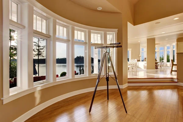Interior of large living room with telescope by large six pane window.