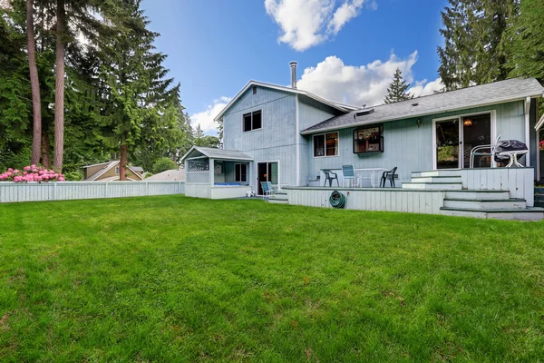 Fenced back yard garden with green grass and small wooden deck