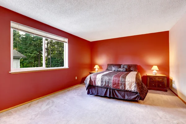 Red bedroom with beige carpet floor and bright colorful bedding.