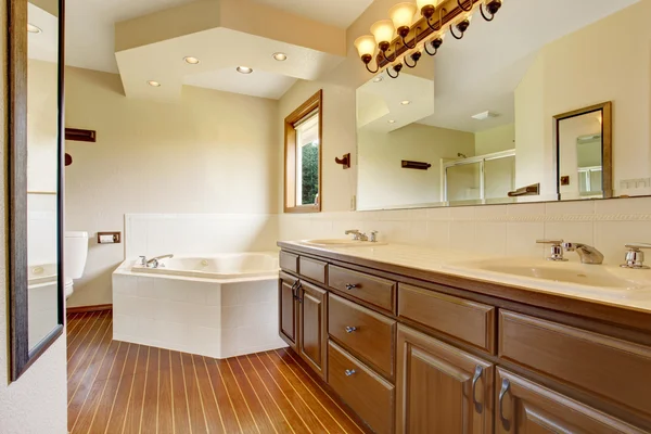 Master bathroom interior with brown cabinets, large mirror with lights and white bathtub.