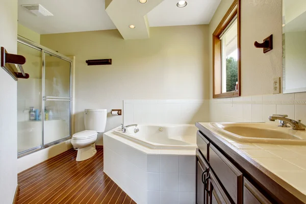 Master bathroom interior with glass shower, hardwood floor and white bathtub with tile trim