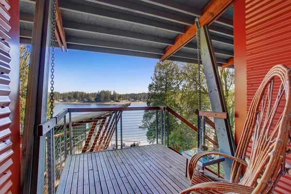 Covered porch of amazing lake house with greenery and a view of the lake.