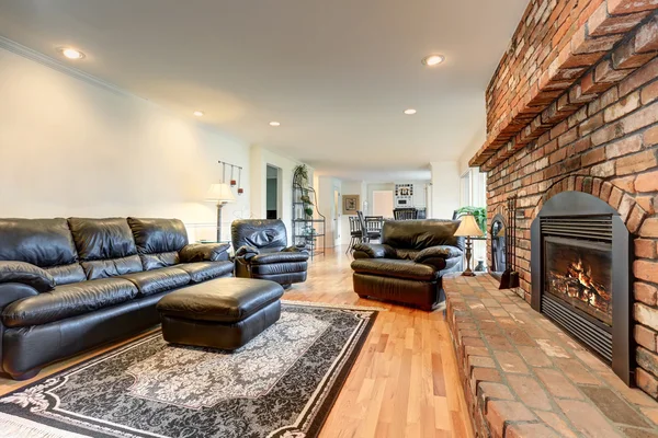 Luxury living room interior with black leather sofa set and brick fireplace.