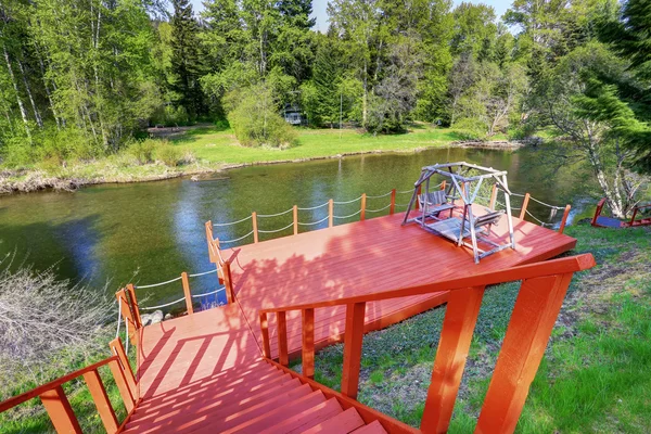 Red walkout deck with staircase on river bank. Backyard view.