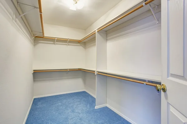 Empty walk-in closet with wood shelves, blue carpet floor.