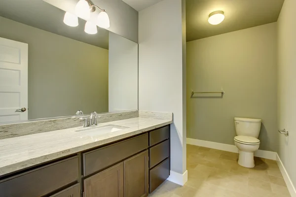 Light bathroom interior with tile floor and vanity cabinet with large mirror.