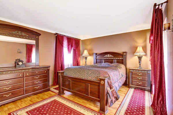 Vintage bedroom interior with wooden furniture, red curtains and rugs.