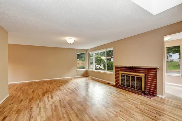 Empty living room interior with brick fireplace and hardwood floor.