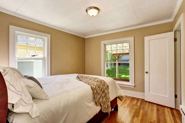 Empty bedroom interior with white bedding and hardwood floor.