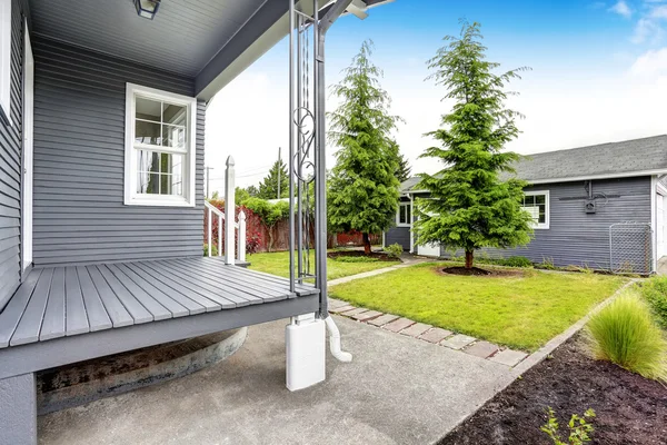 Backyard house with siding trim, wooden floor porch, concrete walkway.