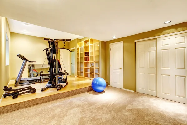 Yellow walls gym room with window. View of exercise equipments.