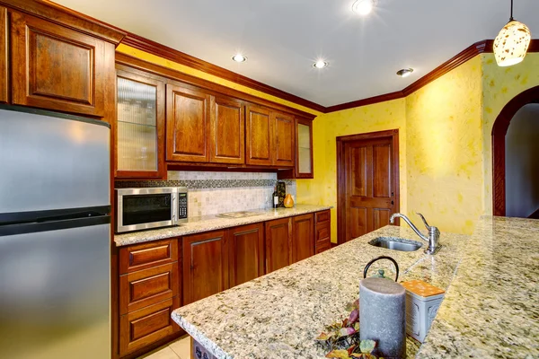 Beautiful cherry wood kitchen with marble counters and tile floor.