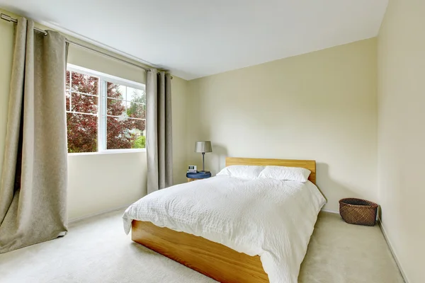 Bedroom interior in light tones with wooden bed and carpet floor.