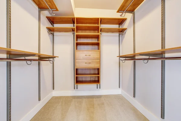 Bright empty walk-in closet with wood shelves, beige carpet floor.