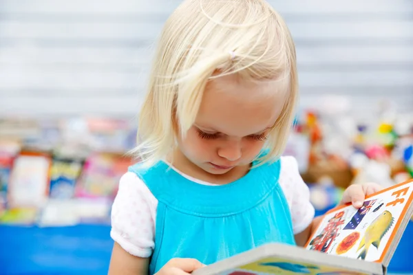 Cute little girl in a blue dress reading a book