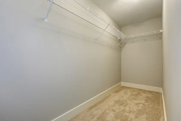 Empty narrow walk-in closet with shelves and carpet floor.