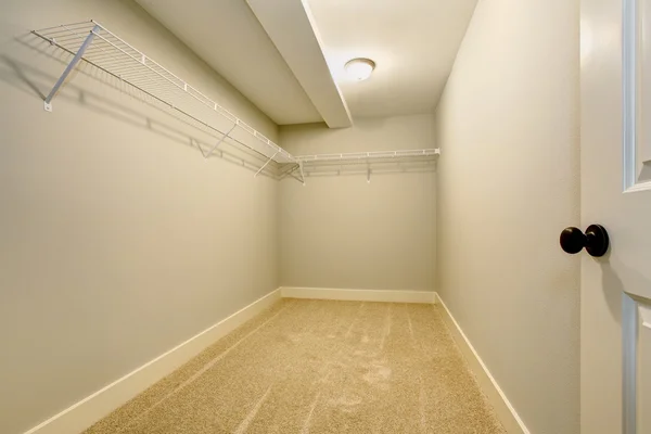 Empty narrow walk-in closet with shelves and carpet floor.