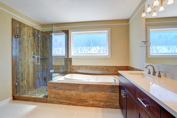 Luxury bathroom interior with large vanity cabinet, glass cabin shower and white bath tub.