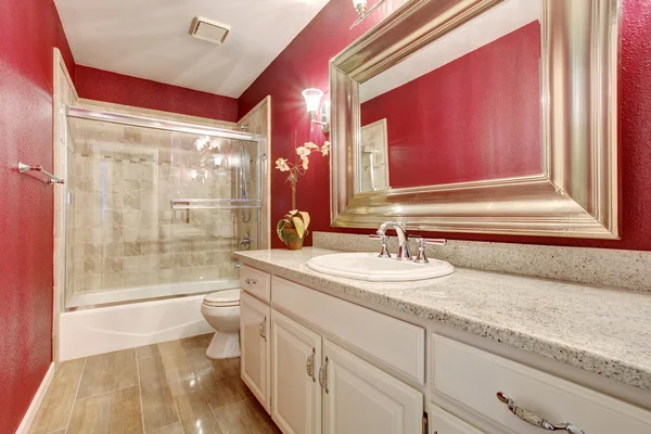 Classy bathroom with red walls, and white cabinets.