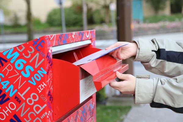 Hand sending a tax report letter in a red mail box