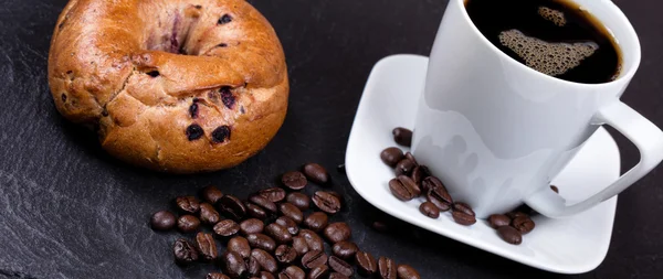 Roasted coffee beans with drink and bagel in background on slate