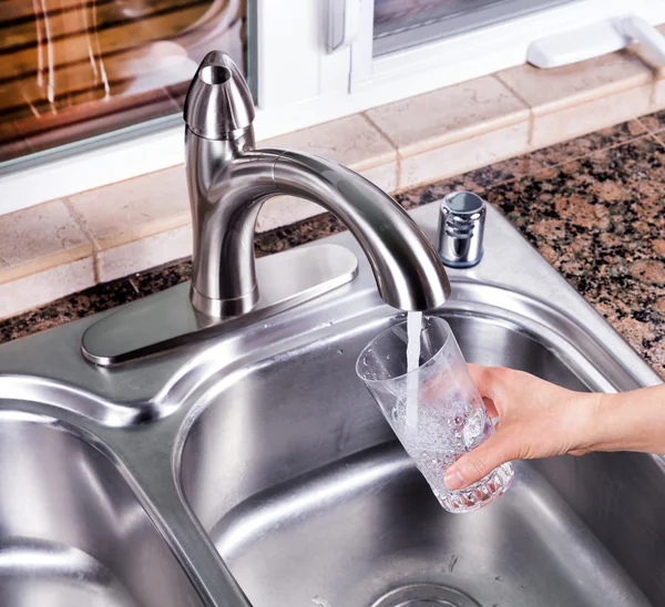 Drinking glass being filled up with tap water from kitchen fauce