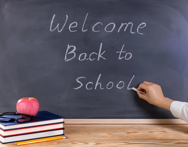 Teacher writing welcome back to school on erased black chalkboar