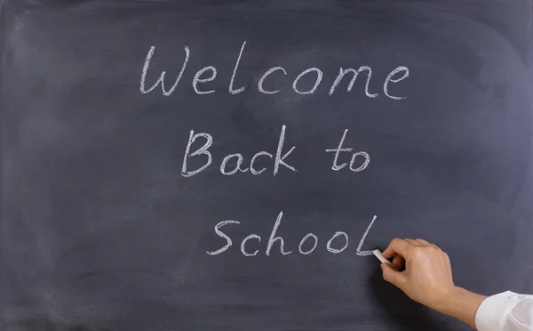 Teacher writing welcome back to school on erased black chalkboar